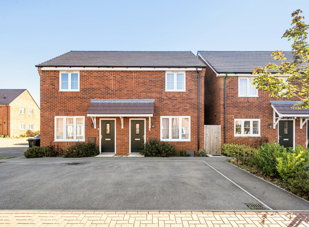 Red-brick semi-detached houses with driveway parking and a small tree outside.