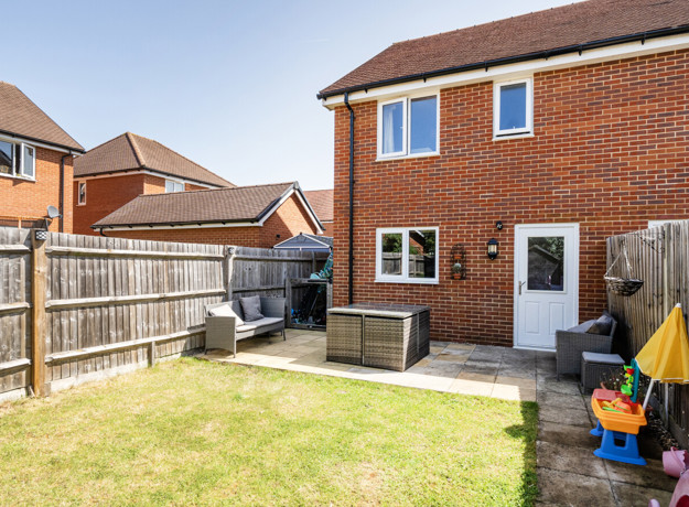 Rear garden with lawn, fence, and brick house exterior view.