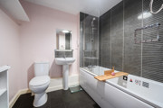 Bathroom with bathtub, wall tiles, toilet and pedestal sink.