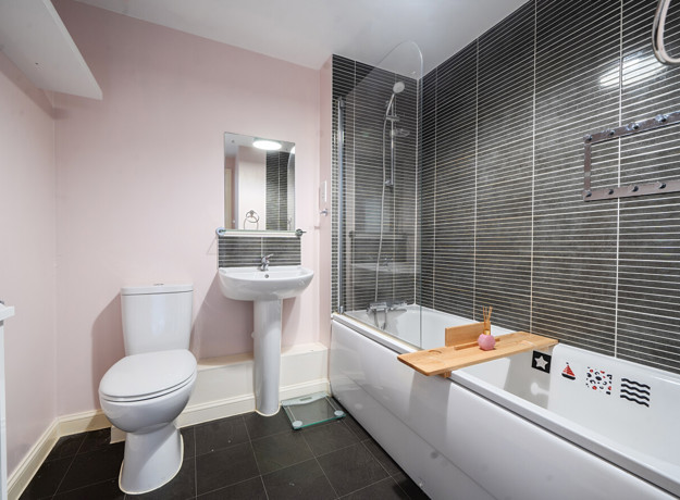 Bathroom with bathtub, wall tiles, toilet and pedestal sink.