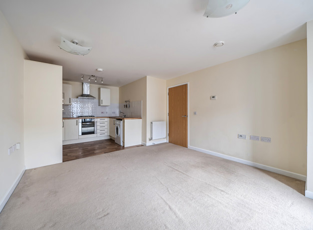 Open-plan living area with fitted kitchen and carpeted floor.