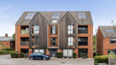 Exterior view of a red brick apartment building with parked cars outside.