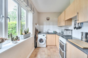 Kitchen with wooden-effect cabinets, dark worktops, sink, appliances, and window.