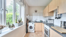 Kitchen with wooden-effect cabinets, dark worktops, sink, appliances, and window.