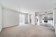 Open-plan living area with carpeted floor and kitchen in the background. (1)