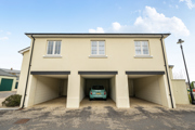 Coach house with cream exterior and three open garages on a paved driveway.
