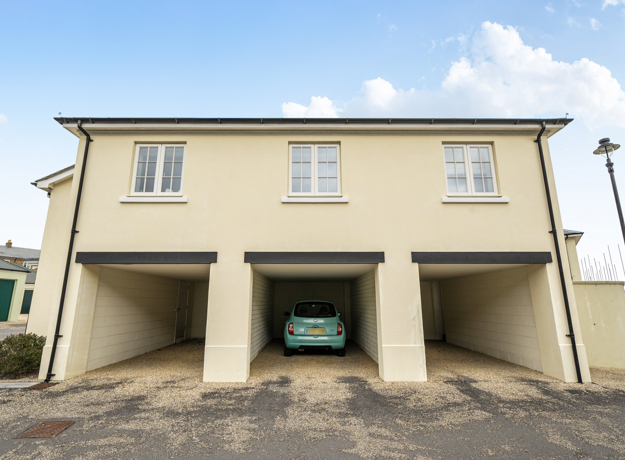 Coach house with cream exterior and three open garages on a paved driveway.