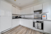 White kitchen with countertop appliances, integrated oven, hob and stainless steel splashback.