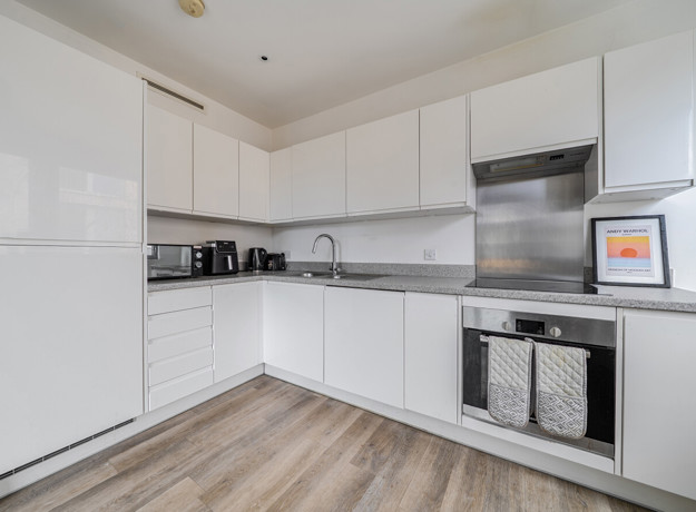 White kitchen with countertop appliances, integrated oven, hob and stainless steel splashback.