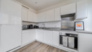 White kitchen with countertop appliances, integrated oven, hob and stainless steel splashback.