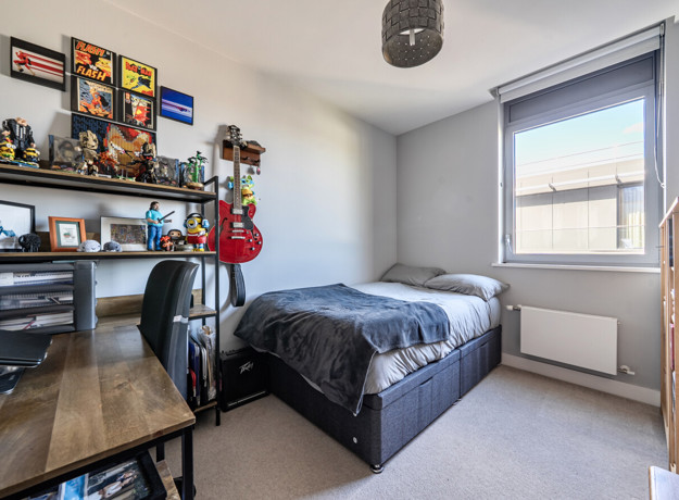 Carpeted bedroom with double bed, desk, shelving and window.