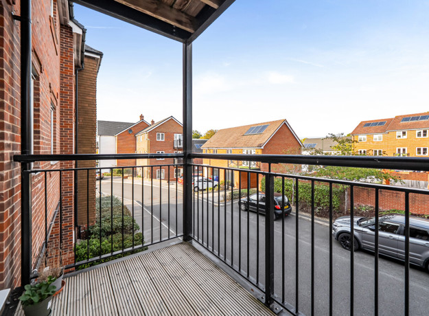Balcony with metal railings overlooking a street and nearby residential buildings.