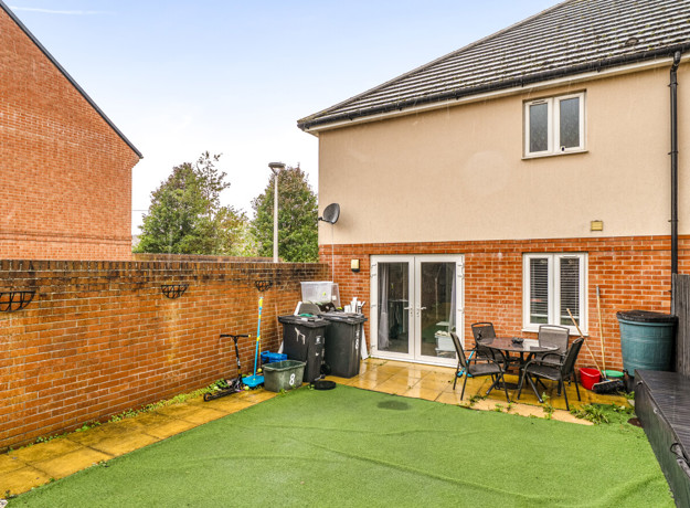 Rear garden with artificial lawn, patio area and fenced boundaries.