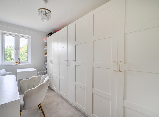 Third bedroom with white wardrobes, desk, chair, and window at the end.
