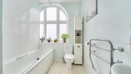 Bathroom with bathtub, toilet, sink, towel rail, and tiled walls with window.