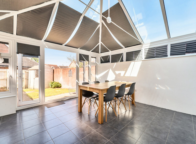 Conservatory with glass roof, tiled floor, and wooden dining table with chairs.