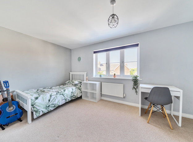 Bedroom with single bed, desk by window, and blue guitar on the floor.