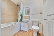 Modern bathroom featuring a bath with shower attachment, wash basin, toilet, and tiled walls.