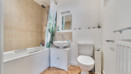 Modern bathroom featuring a bath with shower attachment, wash basin, toilet, and tiled walls.