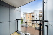 Balcony with glass railing overlooking a road and apartment buildings.