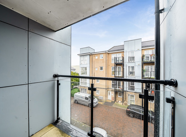 Balcony with glass railing overlooking a road and apartment buildings.