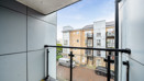 Balcony with glass railing overlooking a road and apartment buildings.