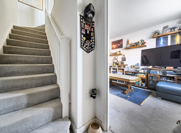 Carpeted staircase with white walls, door leading into living space and landing above.