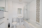 Bathroom with bathtub, shower screen, toilet, sink, and tiled wall.
