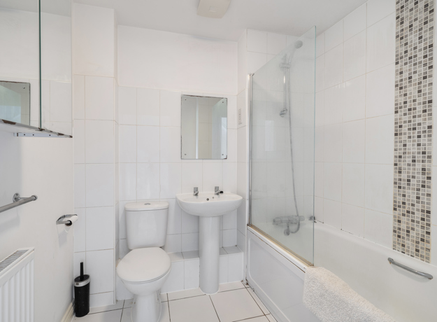 Bathroom with bathtub, shower screen, toilet, sink, and tiled wall.