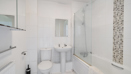 Bathroom with bathtub, shower screen, toilet, sink, and tiled wall.