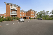 Apartment block with parking spaces, brick facade, and surrounding trees.