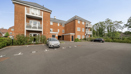 Apartment block with parking spaces, brick facade, and surrounding trees.