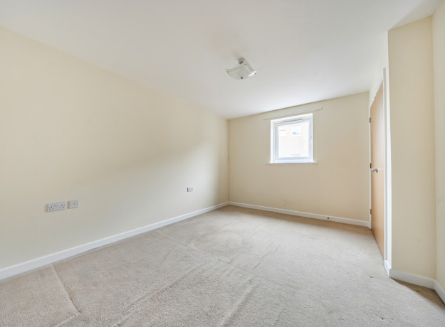 Bedroom with window, carpeted floor and built-in wardrobe.