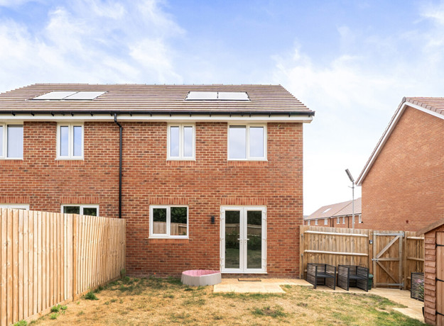 Rear view of the brick house with fenced garden and paved patio area.