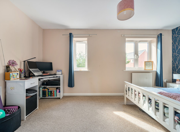 Bedroom with desk, monitors, two windows with curtains and featured wall.