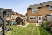 Rear garden with lawn, seating area, shrubs and shed.