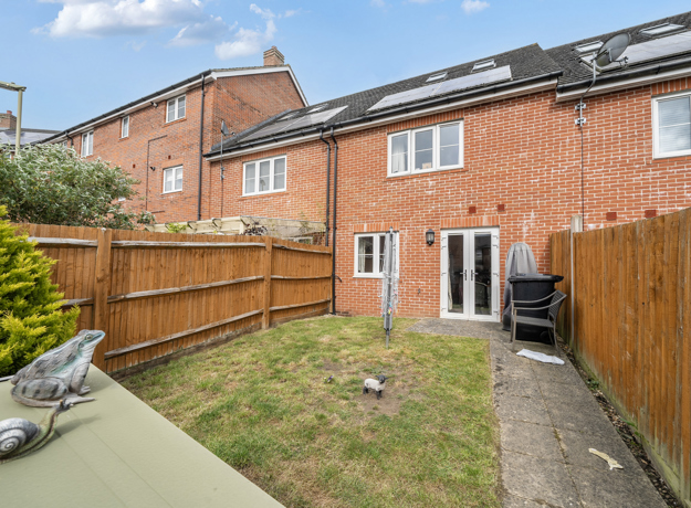 Back garden with grass, fence, patio path, and outdoor storage items.