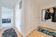 Entrance hallway with wood-effect flooring, storage cupboards, coat hooks, and a view towards the living room.