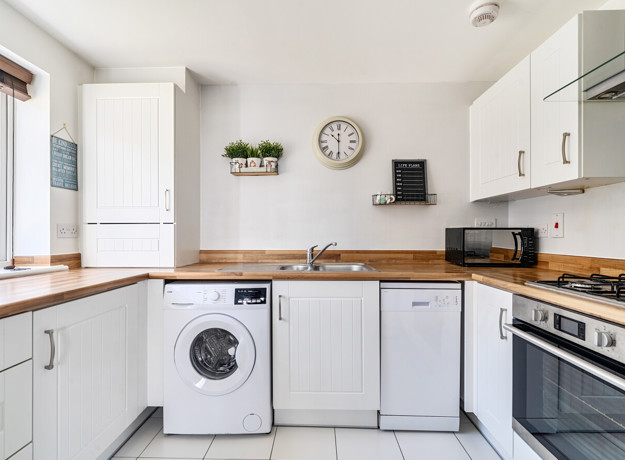 White kitchen with wooden-effect worktops and integrated appliances.