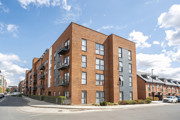 Exterior view of a brick apartment building on a street corner under blue skies.