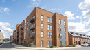 Exterior view of a brick apartment building on a street corner under blue skies.