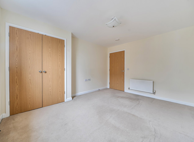 Bedroom with built-in wardrobe, radiator and carpeted floor.