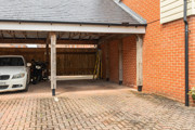 Carport with parked vehicle, brick walls, and paved driveway.
