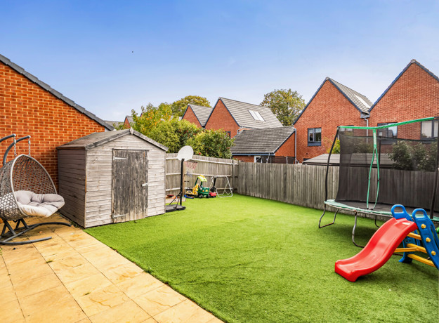 Rear garden with lawn, patio, shed and children's trampoline and slide.