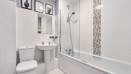 Bathroom with white suite, tiled walls, bathtub, and overhead shower.