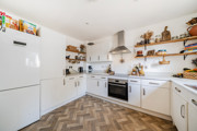 White kitchen with fitted units, open shelving and integrated oven.