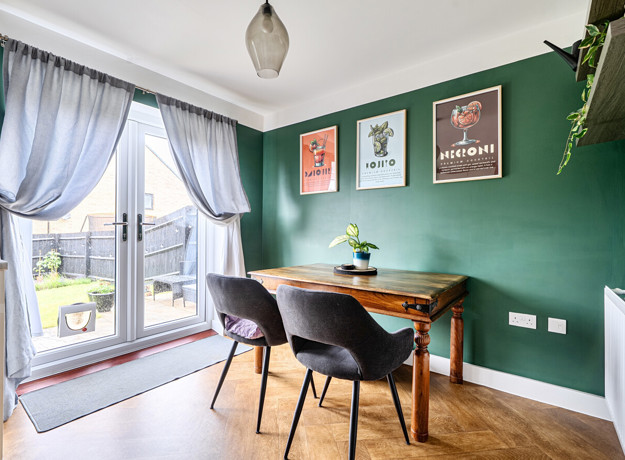 Dining area with table and chairs near french doors with curtains and green wall.