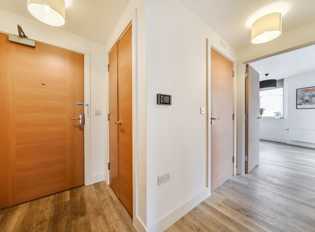 Hallway with wooden entrance door and view towards living area.