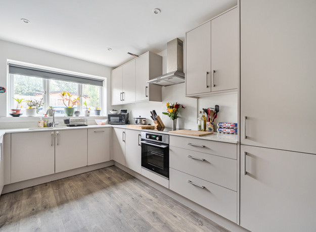 Kitchen with white cabinets, integrated oven and window above the sink.