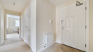 Hallway with doors, radiator, and light walls leading through home.